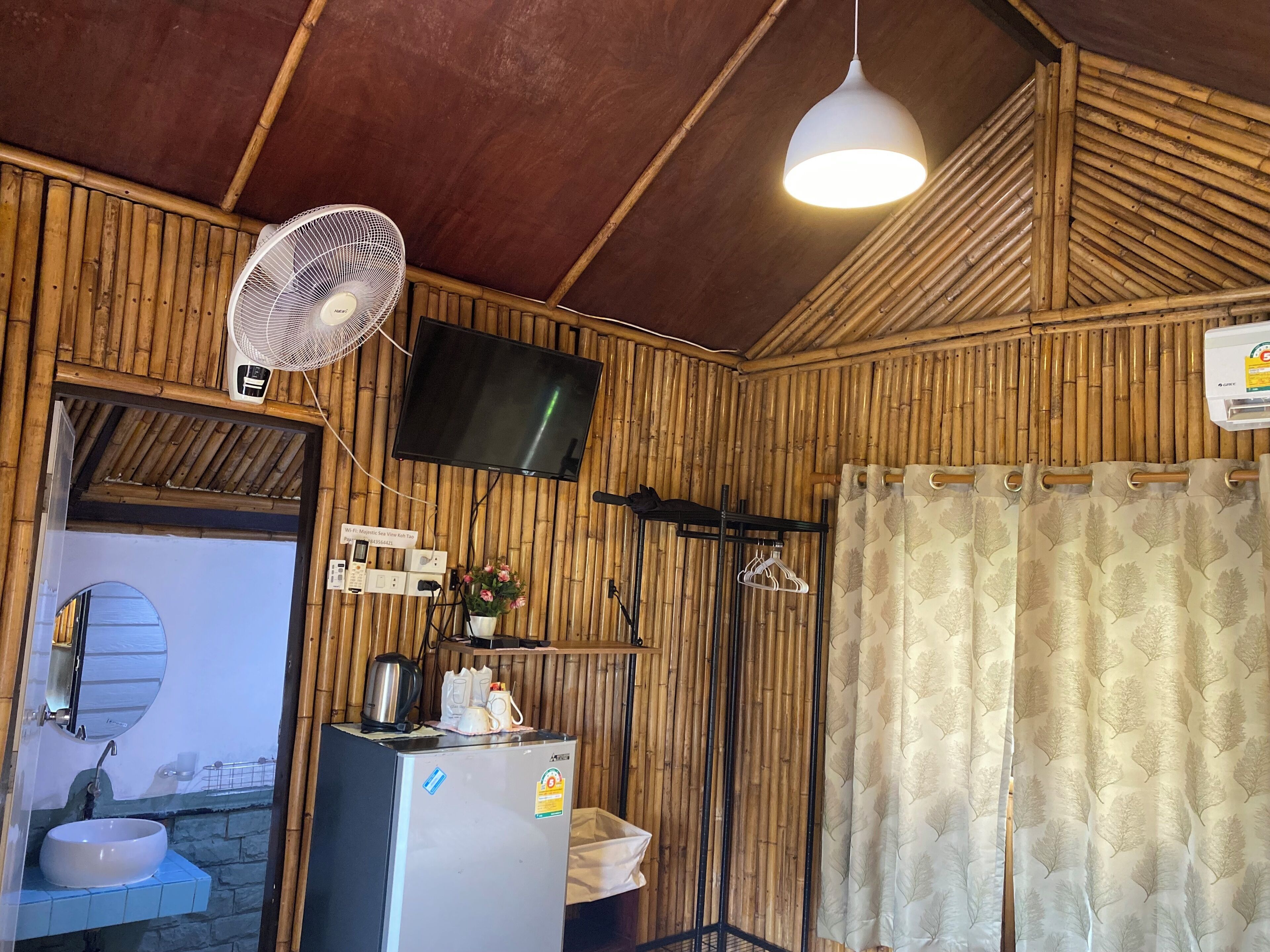 A room with a wooden wall, a ceiling fan, a TV mounted on the wall, a refrigerator, a sink, and a shower curtain.
