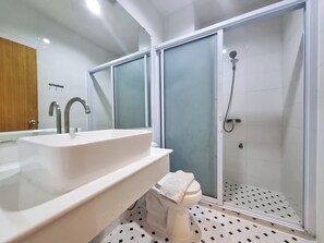 Ett modernt badrum med en stor, vit tvättställ, en spegel och en duschhörna med glasväggar.