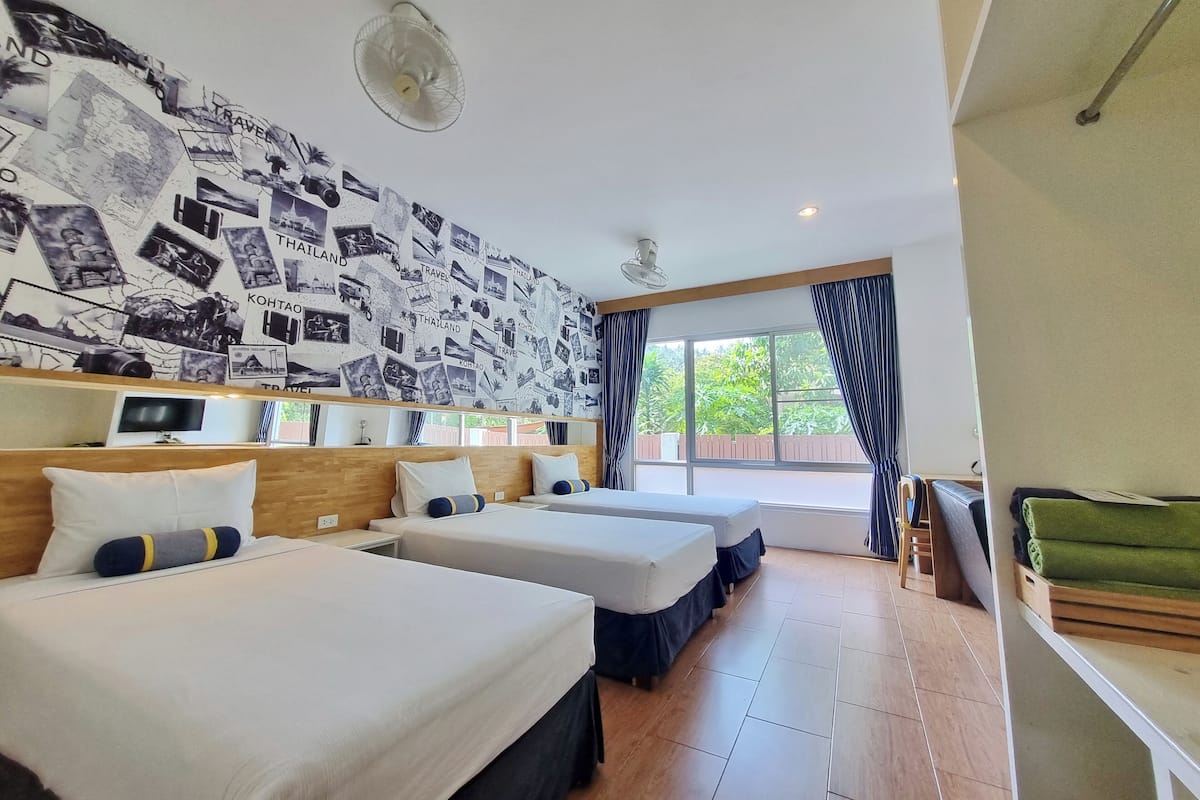 Une chambre d’hôtel avec deux lits, une grande fenêtre avec des rideaux, un mur décoré de photos de voyage et un ventilateur de plafond.