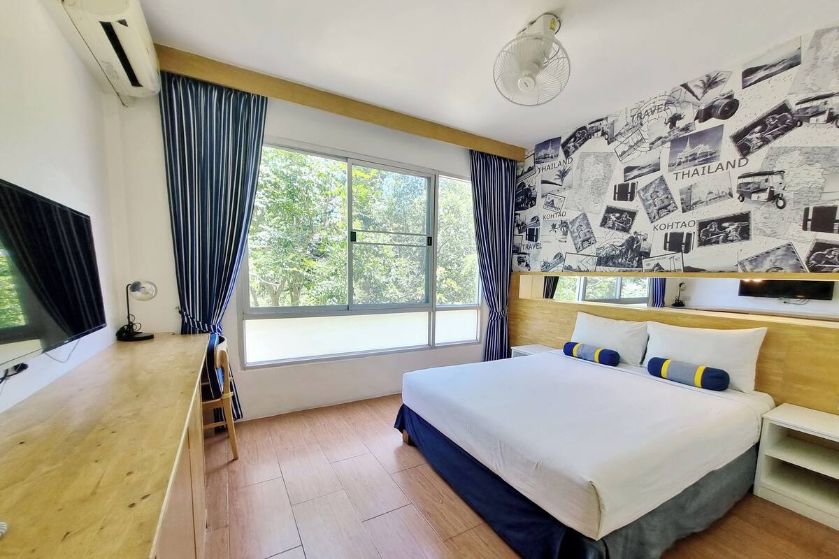 Une chambre d’hôtel avec un grand lit, un bureau doté d’un téléviseur à écran plat, une fenêtre avec des rideaux et un mur décoré de photos de voyage.