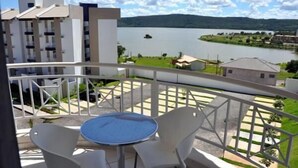 A balcony with a table and chairs, overlooking a lake and buildings. - Enseada Residence (Caldas Novas)
