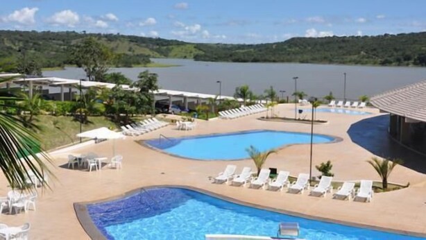 A resort pool area with multiple pools, lounge chairs, and a view of a lake and hills. - Enseada Residence (Caldas Novas)