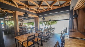 A spacious dining area with wooden tables and chairs, large windows, and a high ceiling with exposed beams.