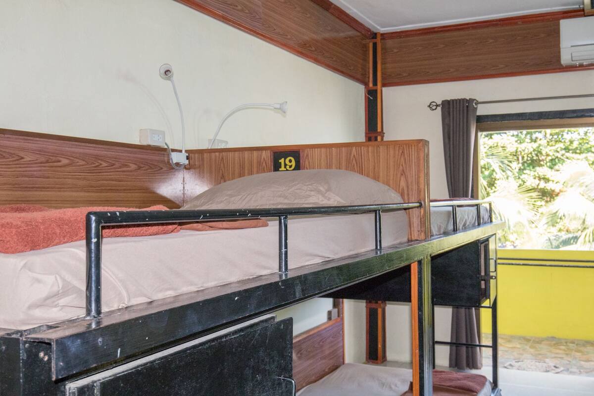 A bunk bed with a headboard labeled '19', a window with curtains, and a view of greenery outside.