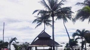 A swimming pool with people in the water, surrounded by palm trees and a thatched-roof structure.
