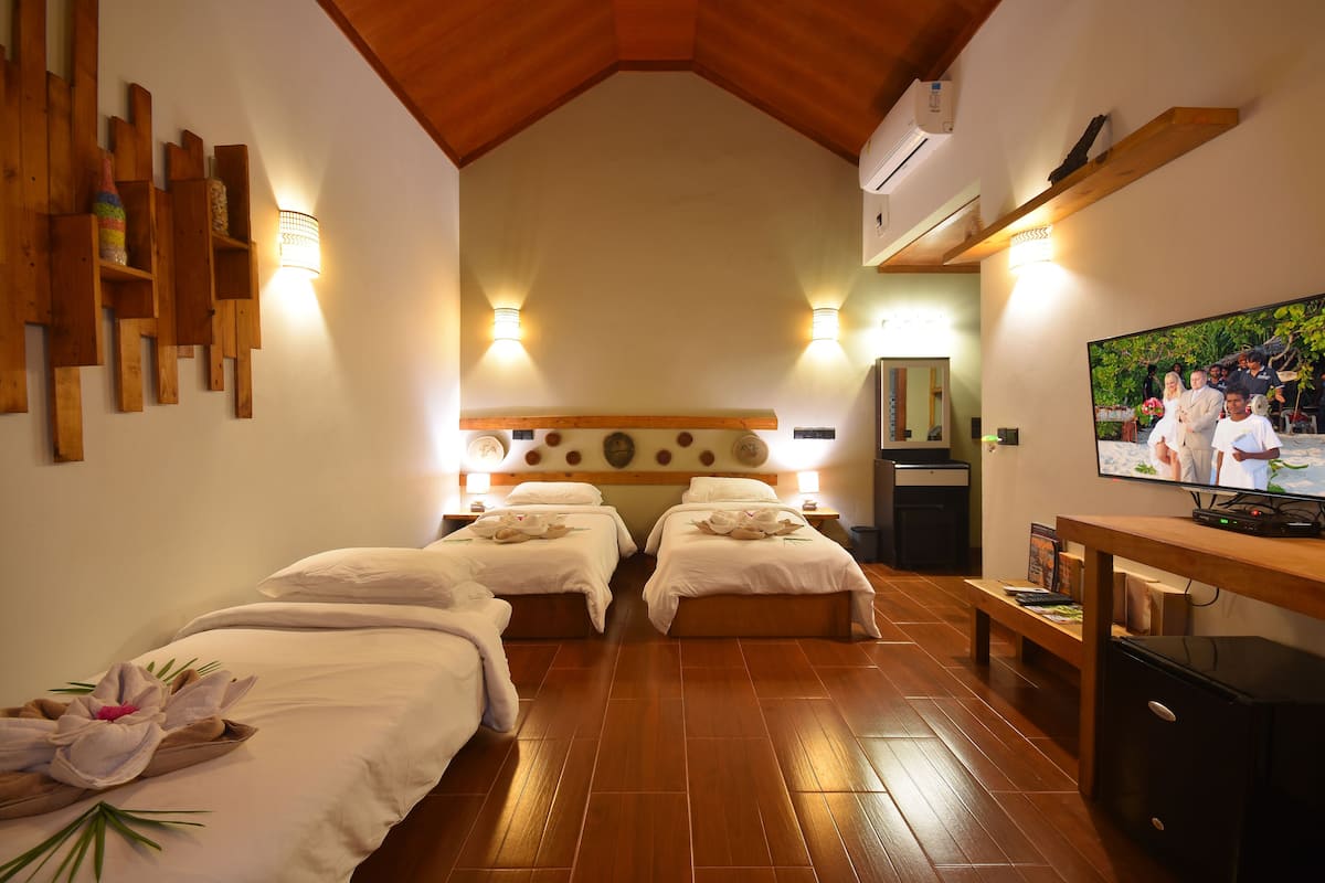 A hotel room with two beds, wooden flooring, a TV, and wall-mounted lights.