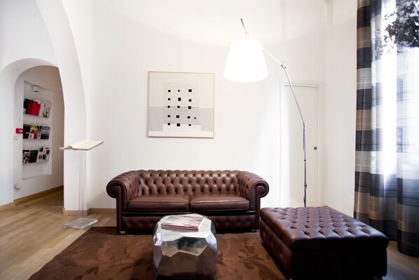 A living room with a brown leather sofa, a matching ottoman, a coffee table, a floor lamp, and a framed abstract artwork on the wall.
