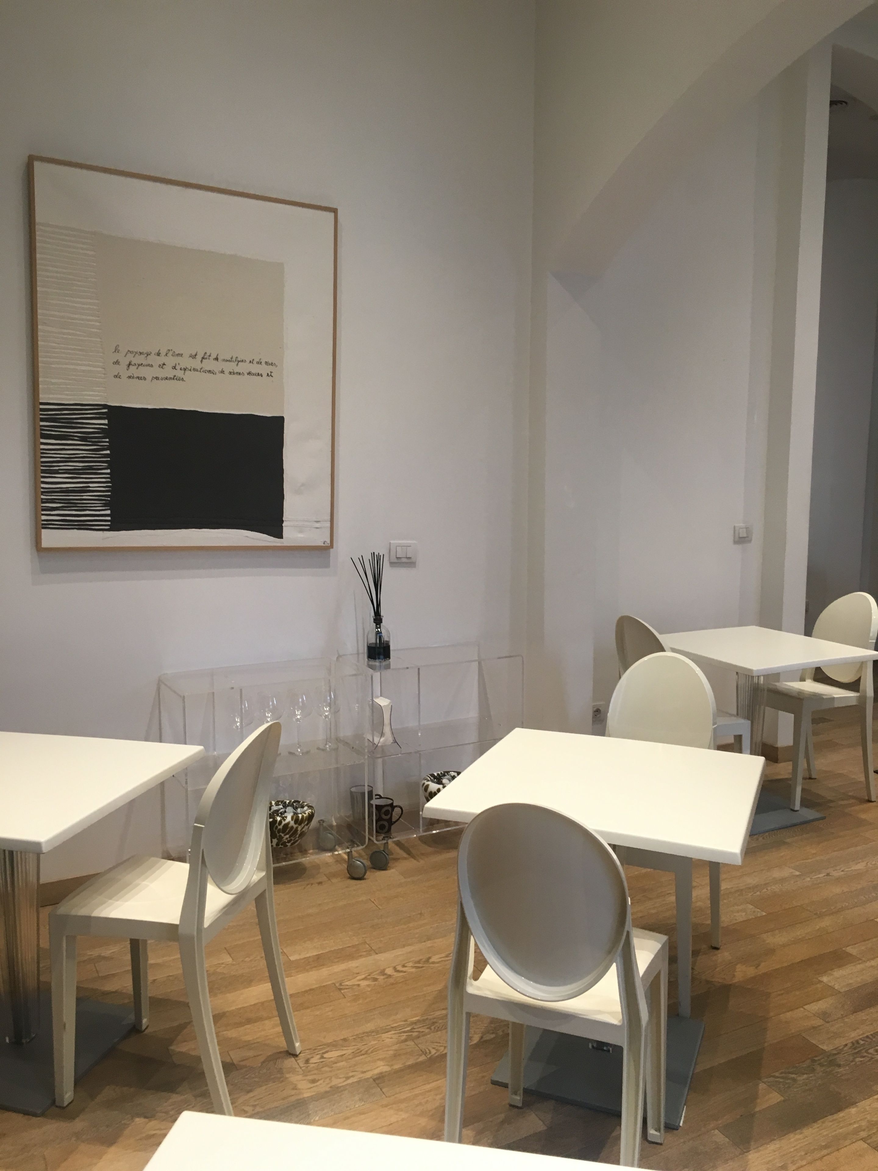 A modern, minimalist room with white tables and chairs, a large abstract painting on the wall, and a clear glass display case with decorative items.