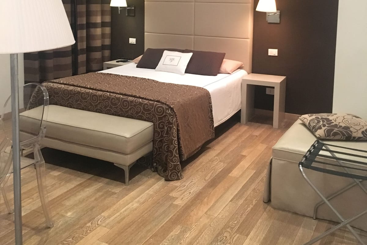 A modern bedroom with a large bed, bedside tables, a bench, and a floor lamp.