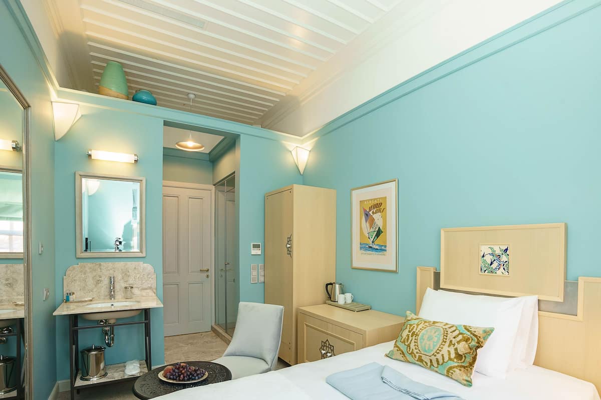 A room with a bed, a bedside table, a mirror, a sink, and a door leading to another room.