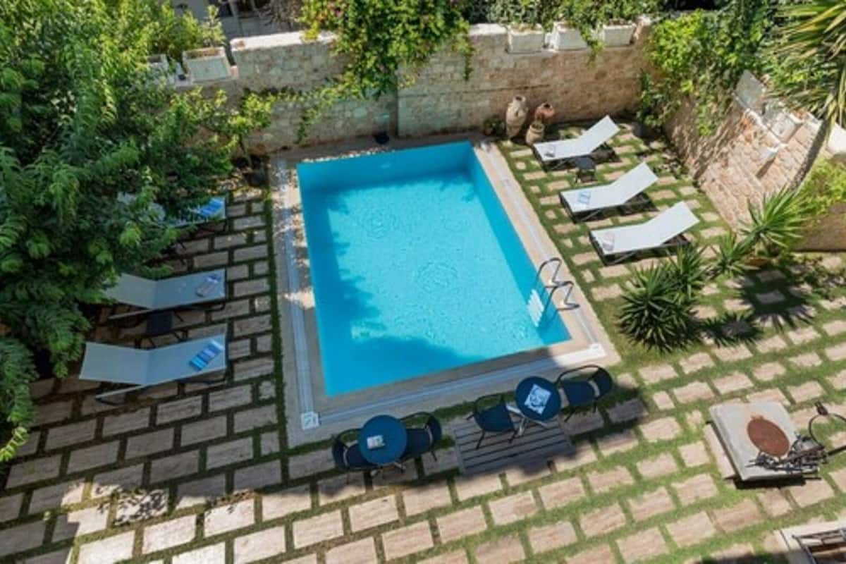 An aerial view of a rectangular swimming pool surrounded by a stone wall, with lounge chairs and tables arranged around the pool.