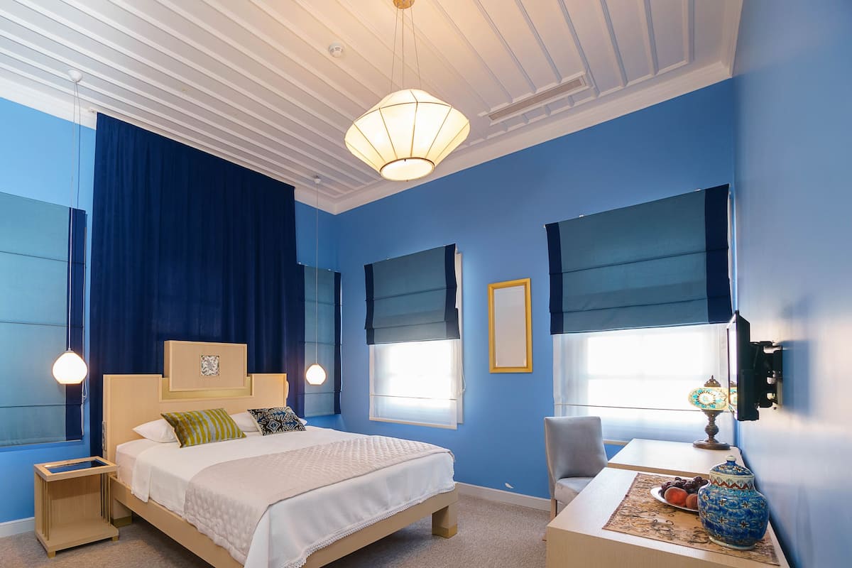 A bedroom with a large bed, bedside tables, a chair, a desk, and a lamp.