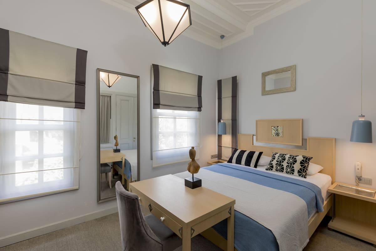 A hotel room with a bed, bedside table, desk, chair, and a large mirror.