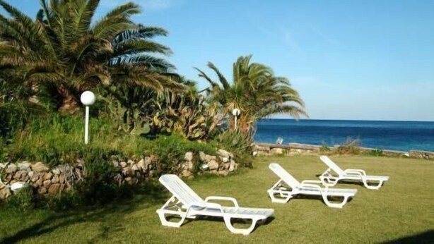 A beachside lounge area with white sun loungers, palm trees, and a clear view of the ocean. - Le Stanze sul Mare (Carini)