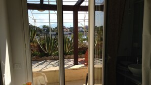 A room with a sliding glass door leading to a balcony. The balcony has a tiled floor and is surrounded by plants and a view of a residential area. - Le Stanze sul Mare (Carini)