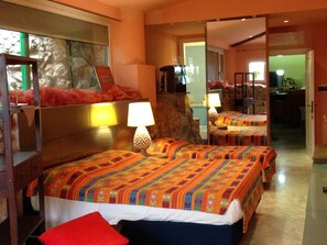 A hotel room with two beds, a mirror, a television, and a stone wall.