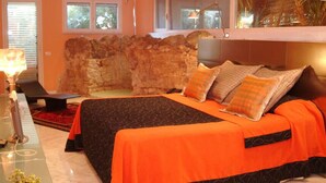 A hotel room with a large bed, a stone wall, a desk with a lamp, and a view of the outdoors. - Le Stanze sul Mare (Carini)