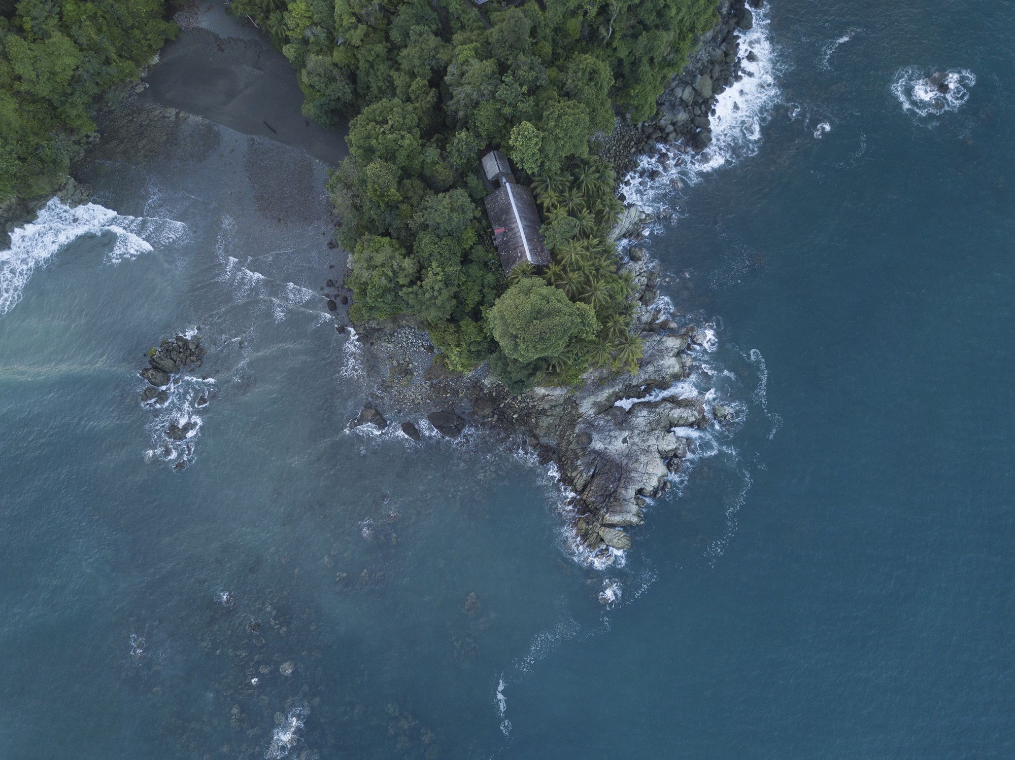An aerial view of a coastal area with a narrow strip of land, dense green vegetation, and rocky terrain.