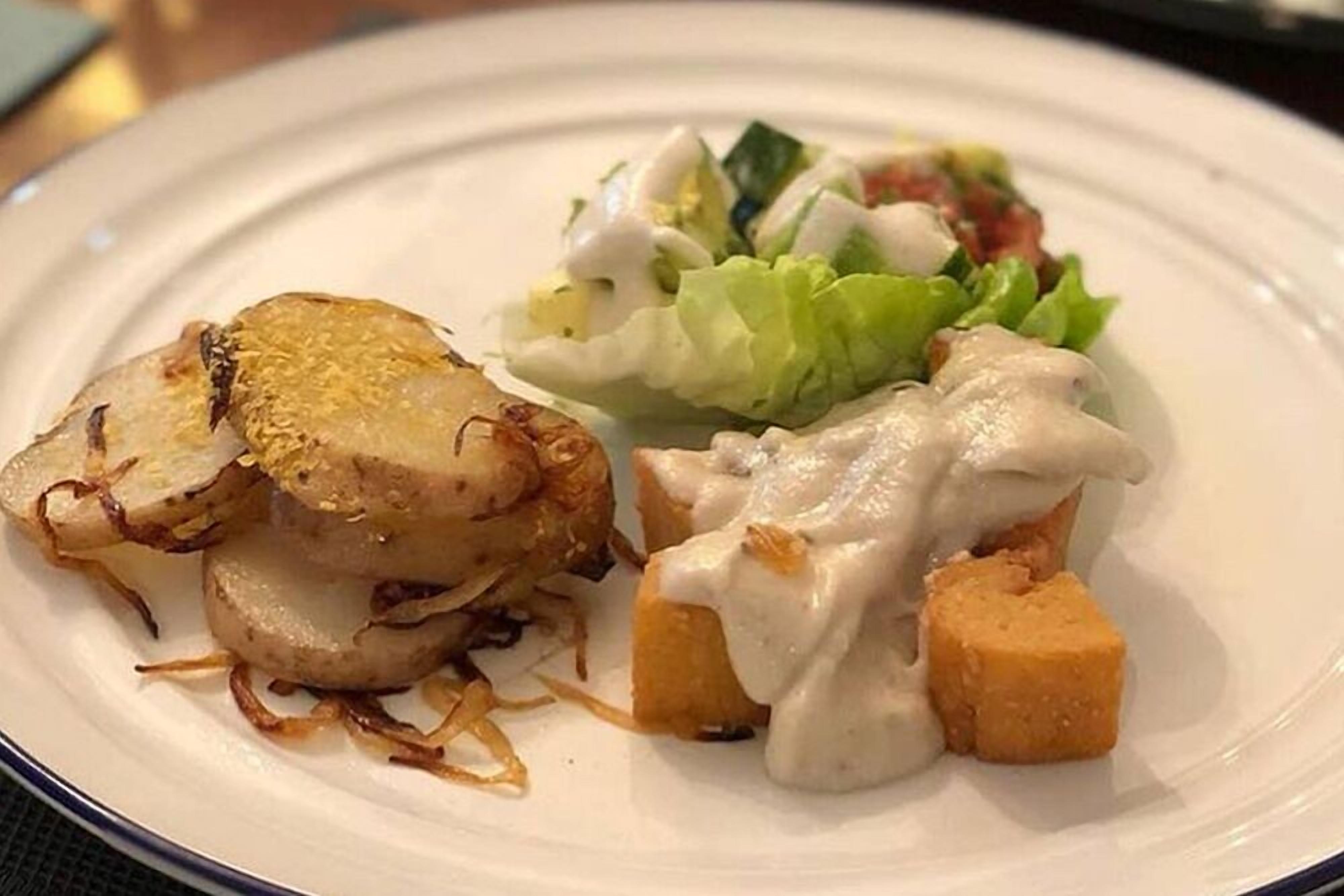 A plate with sliced potatoes, a creamy sauce, and a side salad.