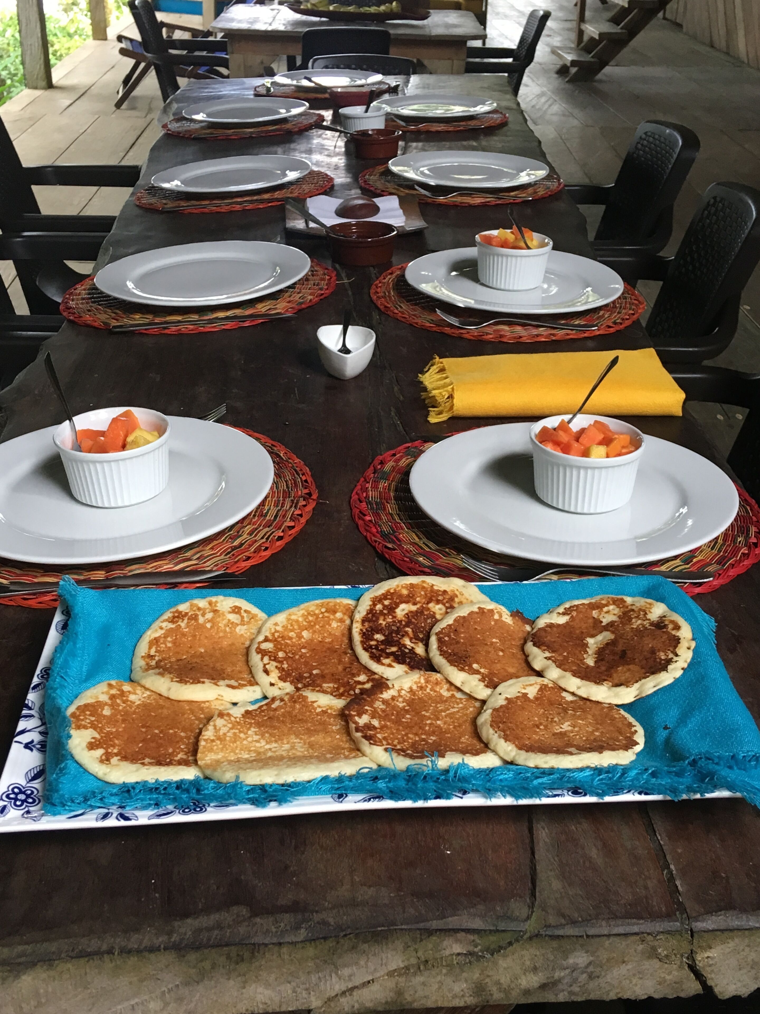 Mesa de jantar posta com pratos, tigelas e uma bandeja de panquecas.