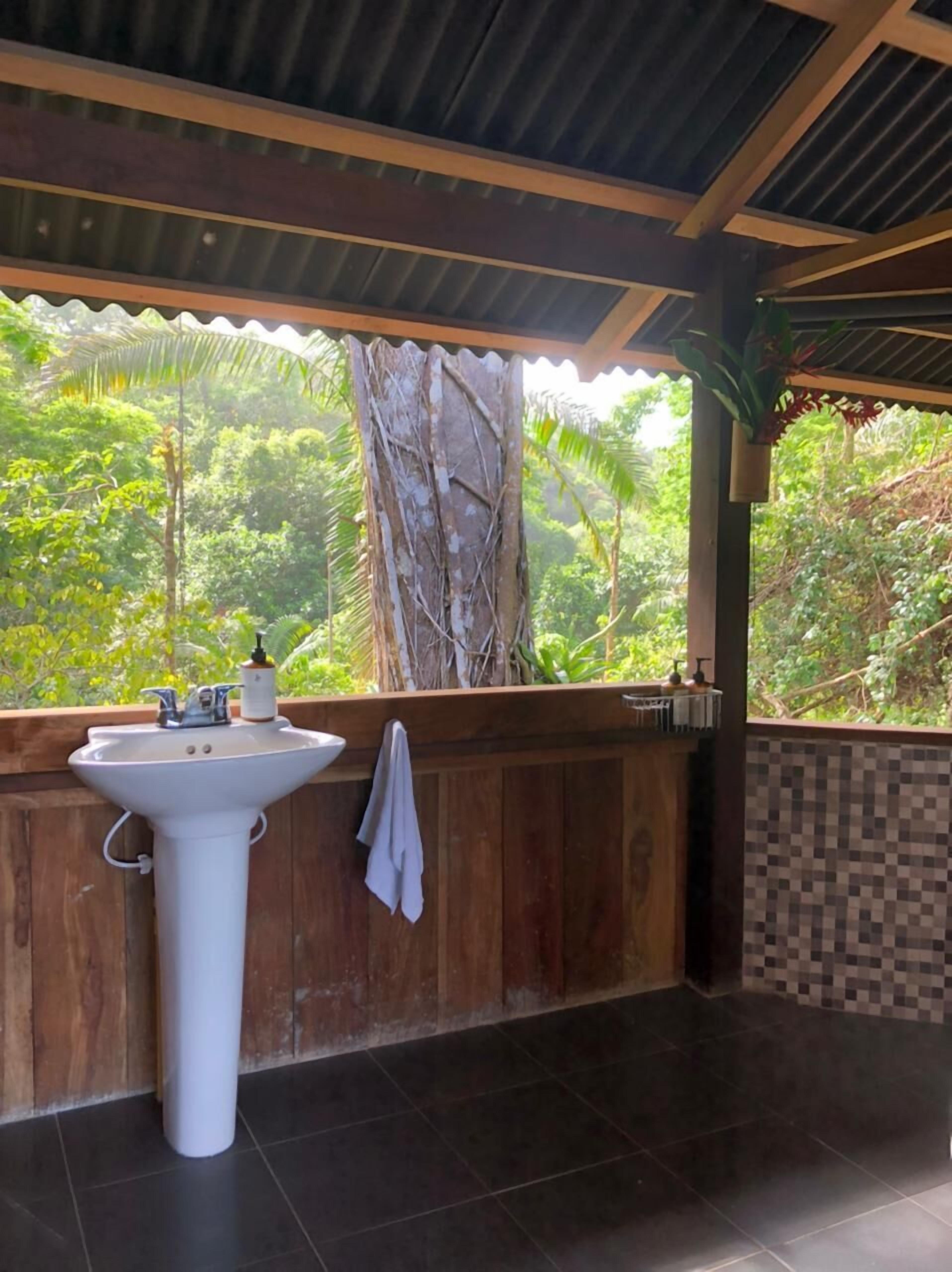 A bathroom with a white sink, wooden walls, and a view of lush greenery.
