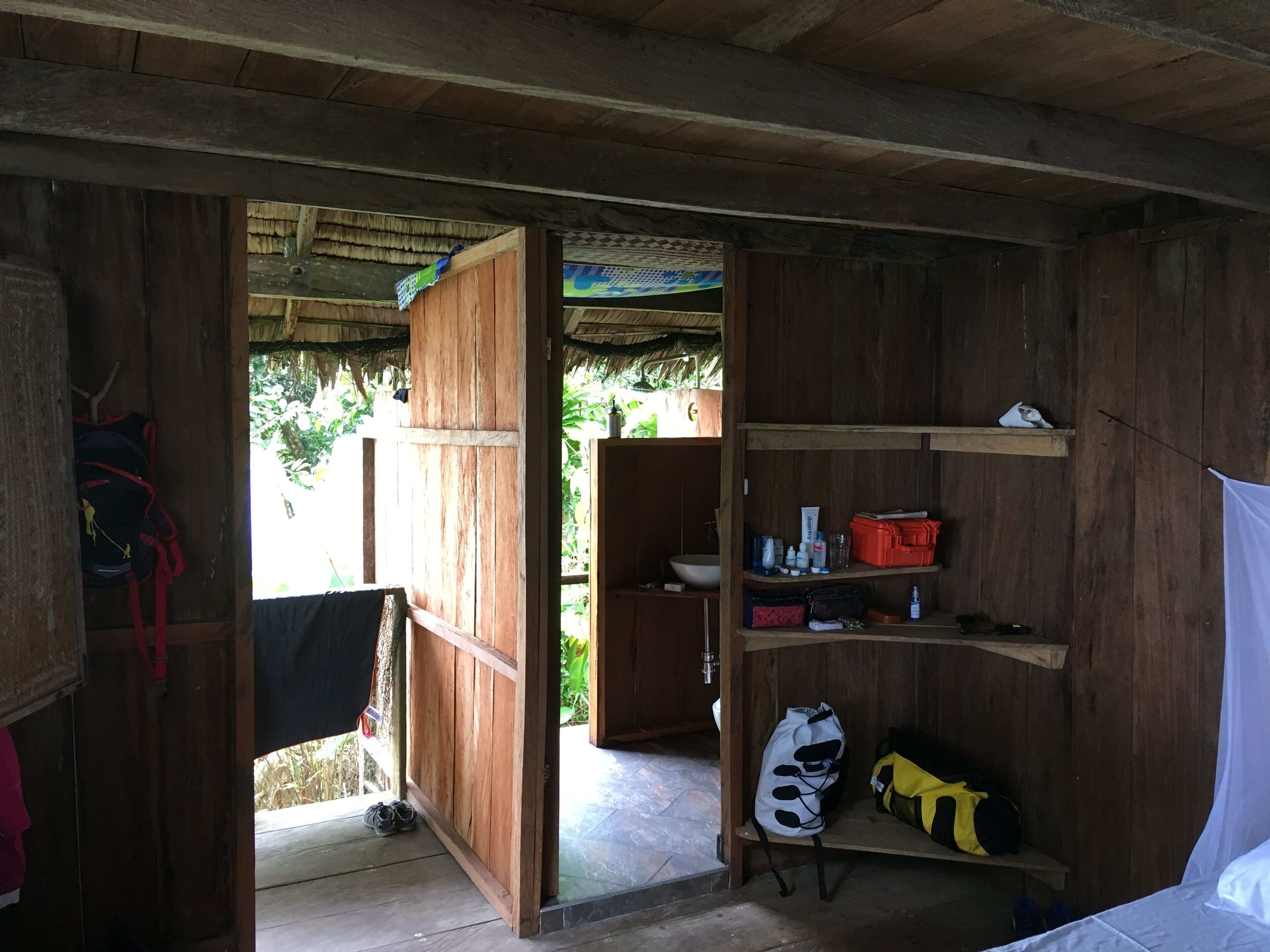 Quarto de madeira com uma cama, um armário com artigos de higiene e uma porta que dá para o exterior.