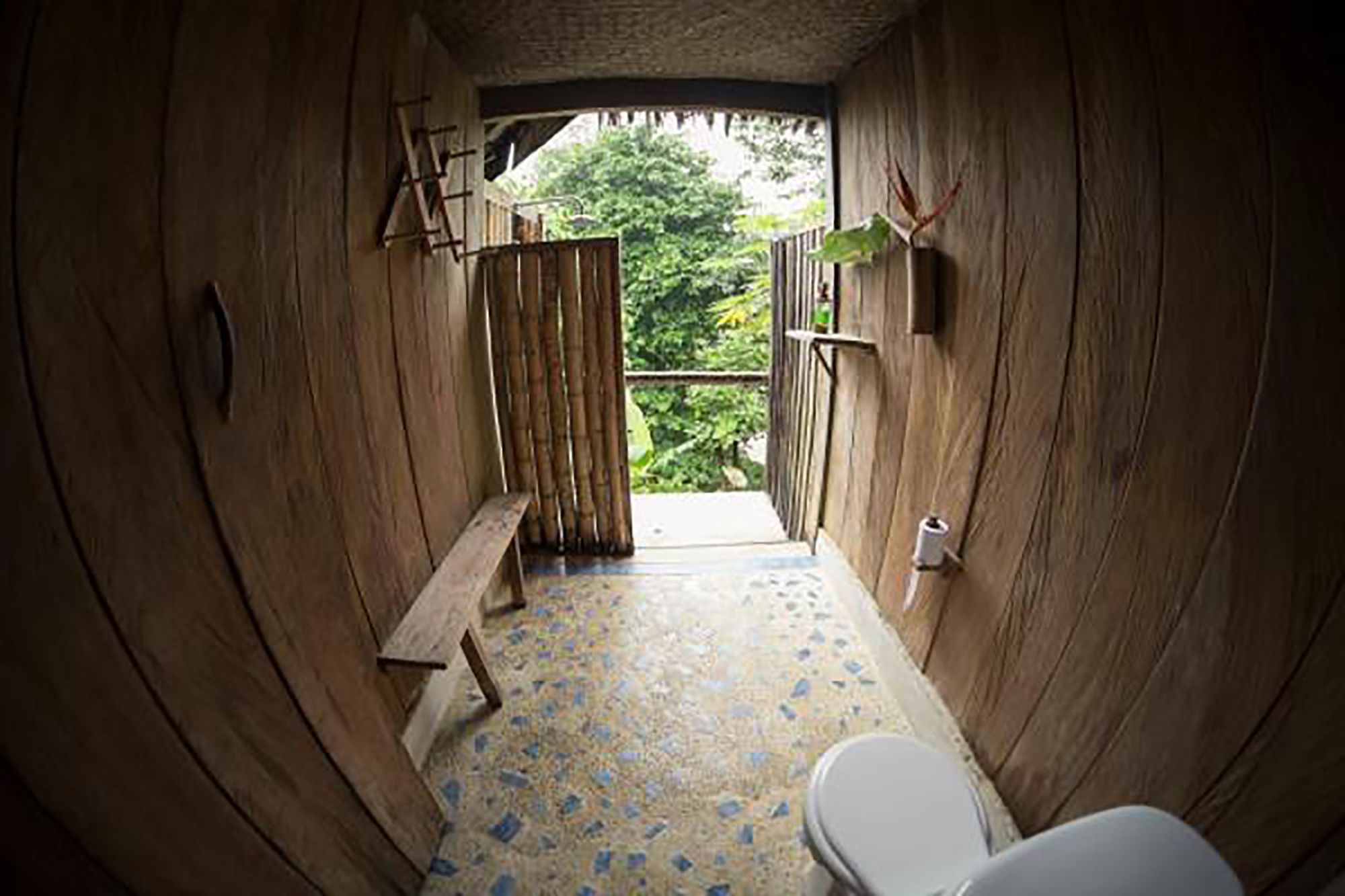 Un cuarto pequeño de madera con un banco, un inodoro y una puerta que da al exterior.