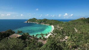 A coastal view with a beach, clear turquoise waters, and lush greenery. - Villas Del Sol Resort (Koh Tao)