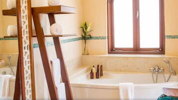 Un baño con bañera, ducha y ventana con vistas. Hay toallas en un perchero y artículos de aseo en el lavabo.