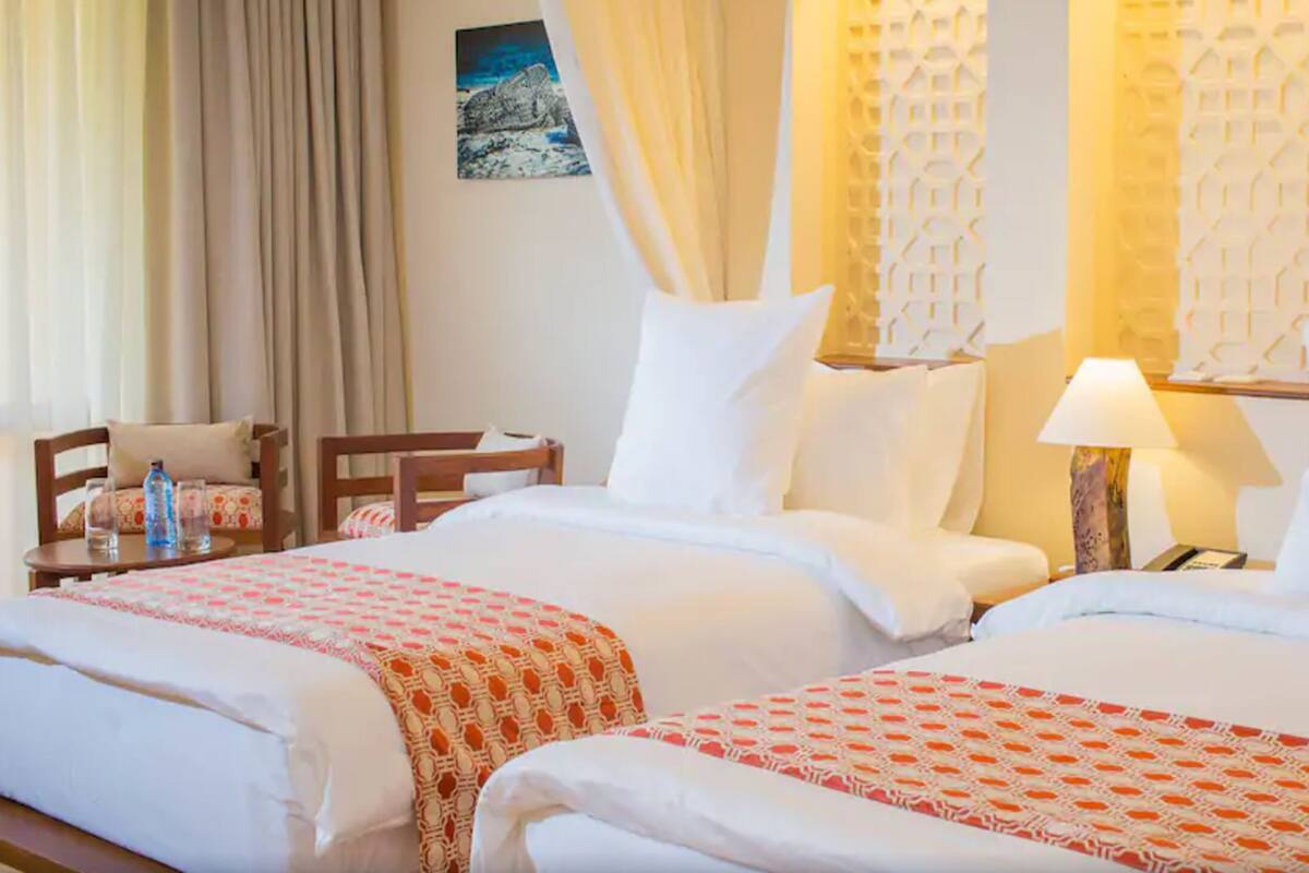 Habitación de hotel con dos camas, un escritorio, una silla y una lámpara.