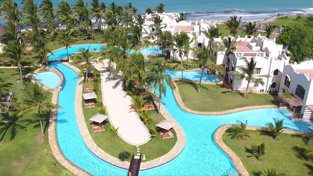 An aerial view of a resort with a winding pool, palm trees, and beachfront villas. - Silver Palm Spa and Resort (Kilifi)