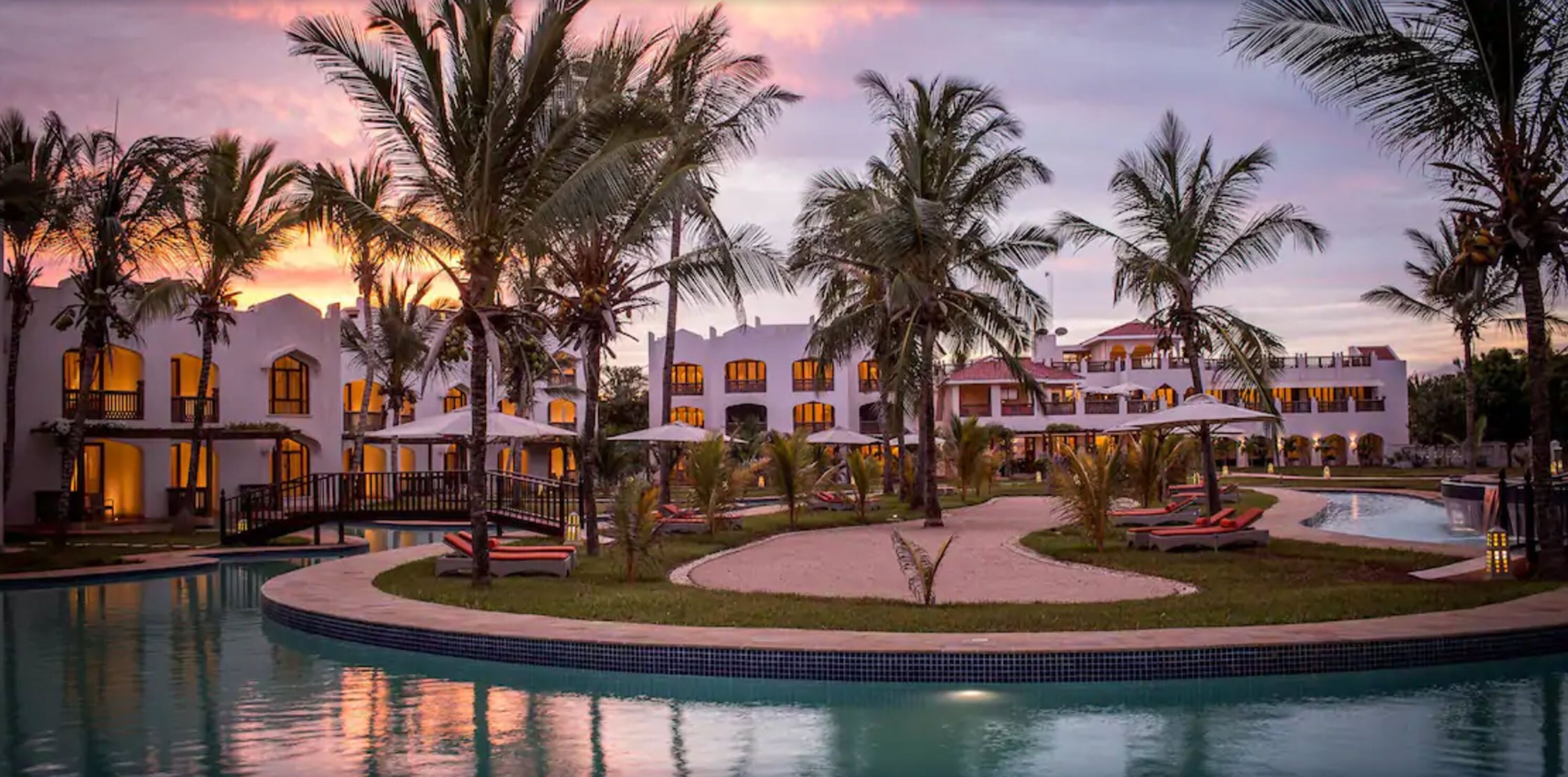 A resort with a swimming pool, palm trees, and a building with multiple balconies.