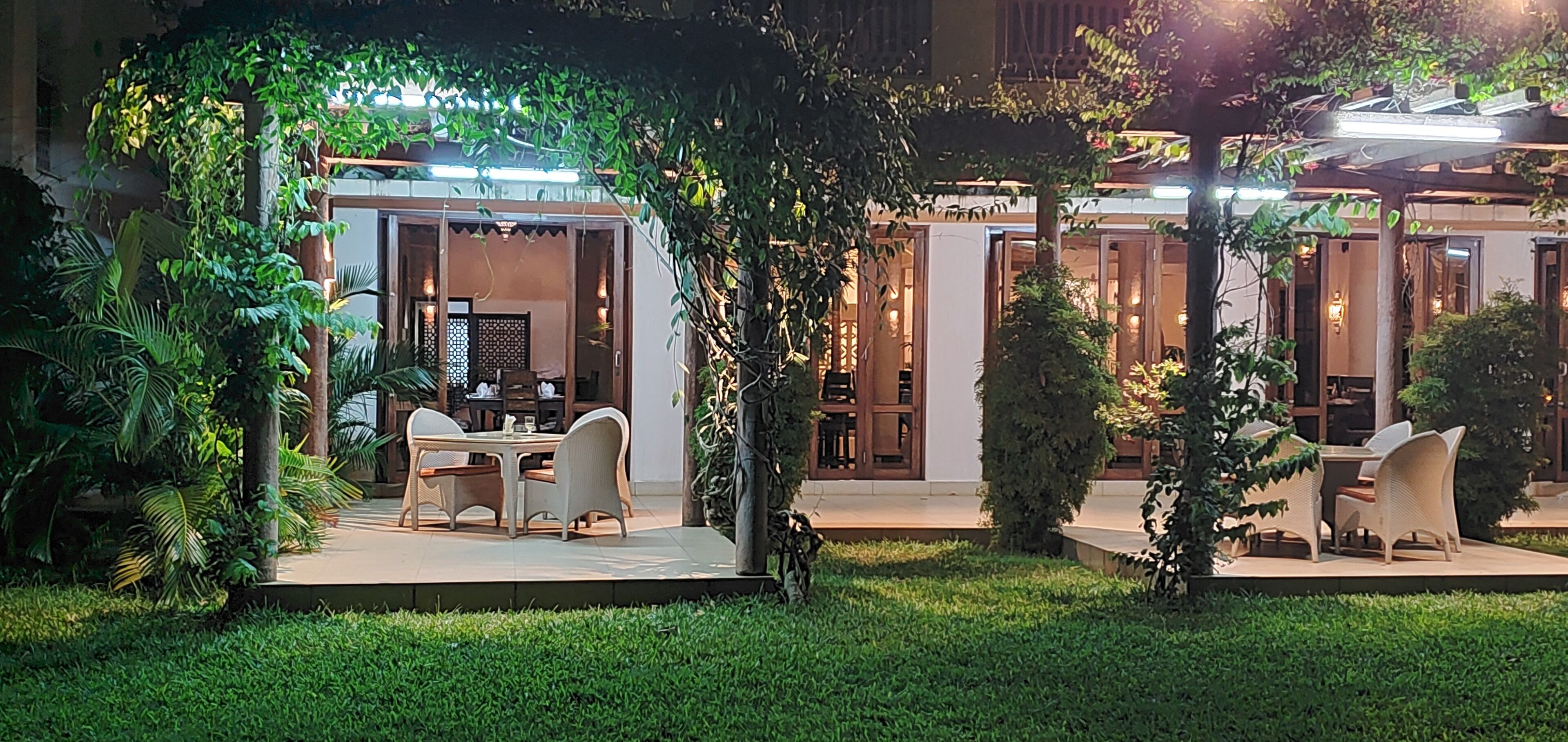 Un patio al aire libre con una mesa y sillas para comer, rodeado de abundante follaje y cubierto por una pérgola.