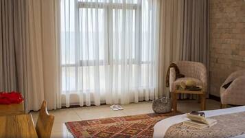 A hotel room with a large window, a bed, a chair, a small table, and a rug.