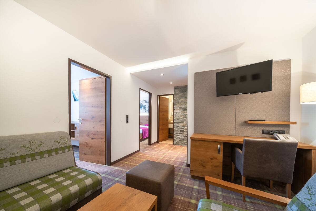 Una habitación de hotel moderna con un sofá, una mesa de madera, un televisor montado en la pared y un piso a cuadros.