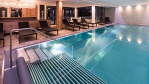 Un área de piscina interior moderna con sillones de descanso, un mostrador de recepción y un amplio ventanal con vistas al cielo nocturno.