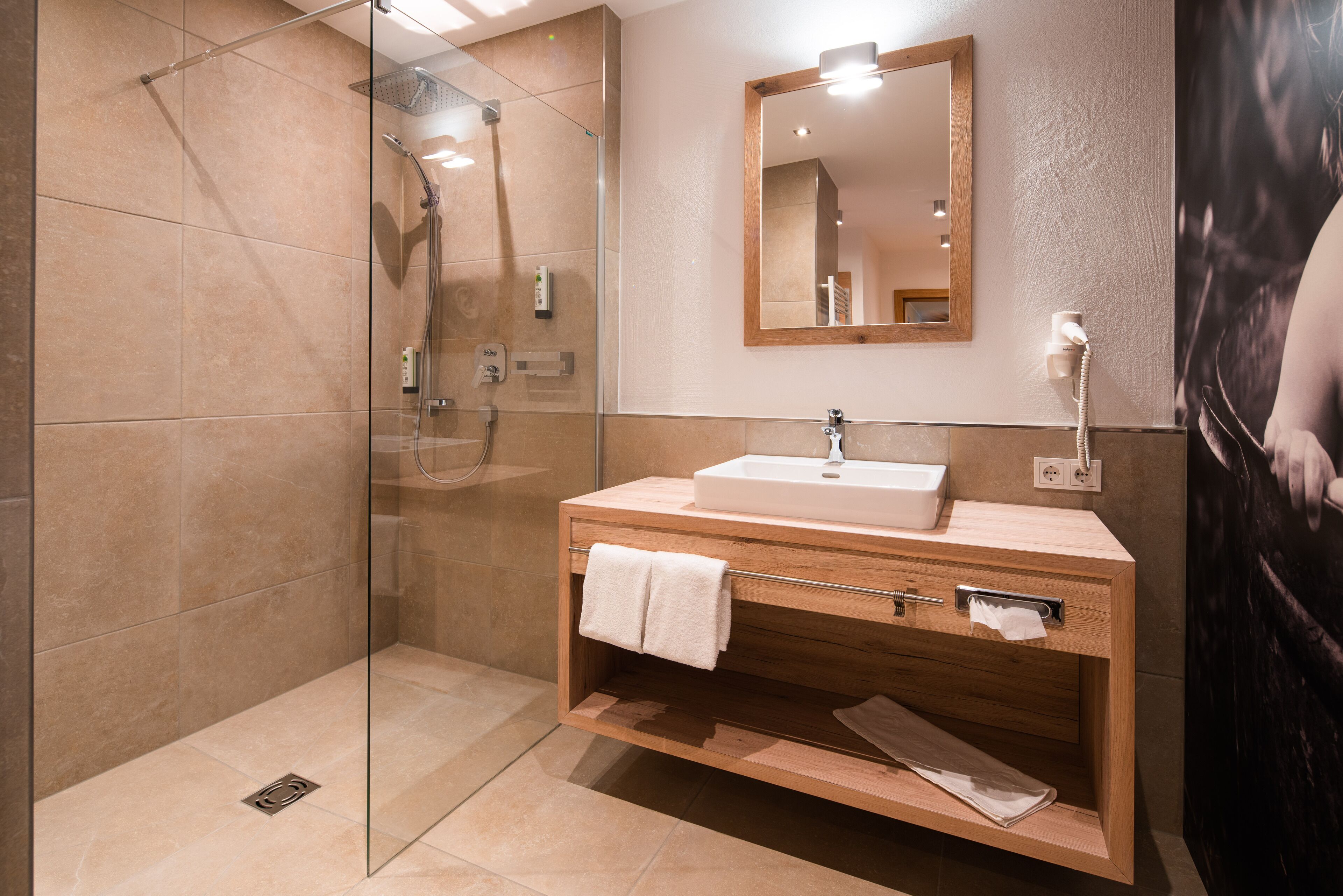 Un baño moderno con ducha de vidrio, tocador de madera con lavamanos y un espejo encima.