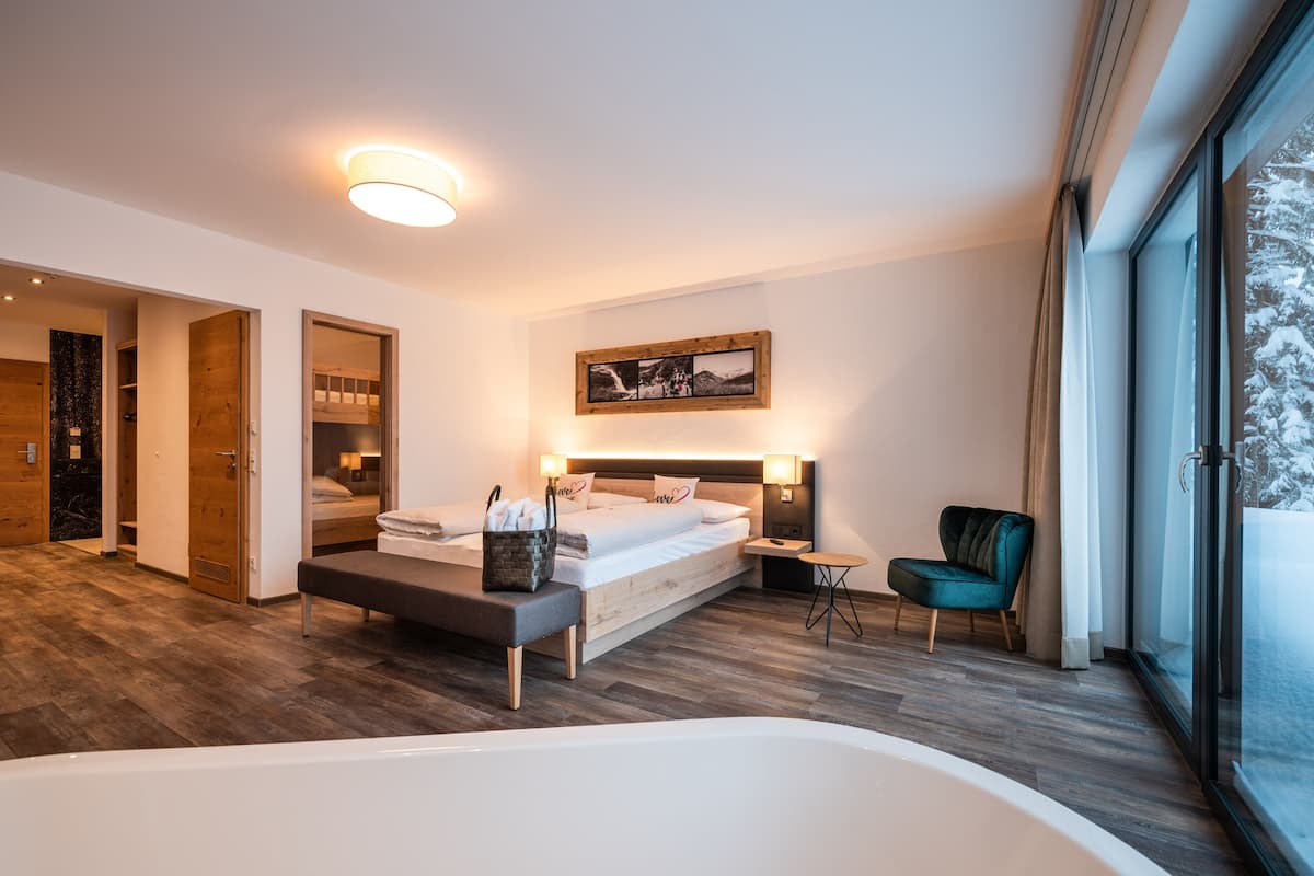 Un dormitorio moderno con una cama grande, una mesita de noche, una silla y vistas a un paisaje nevado a través de un ventanal amplio.
