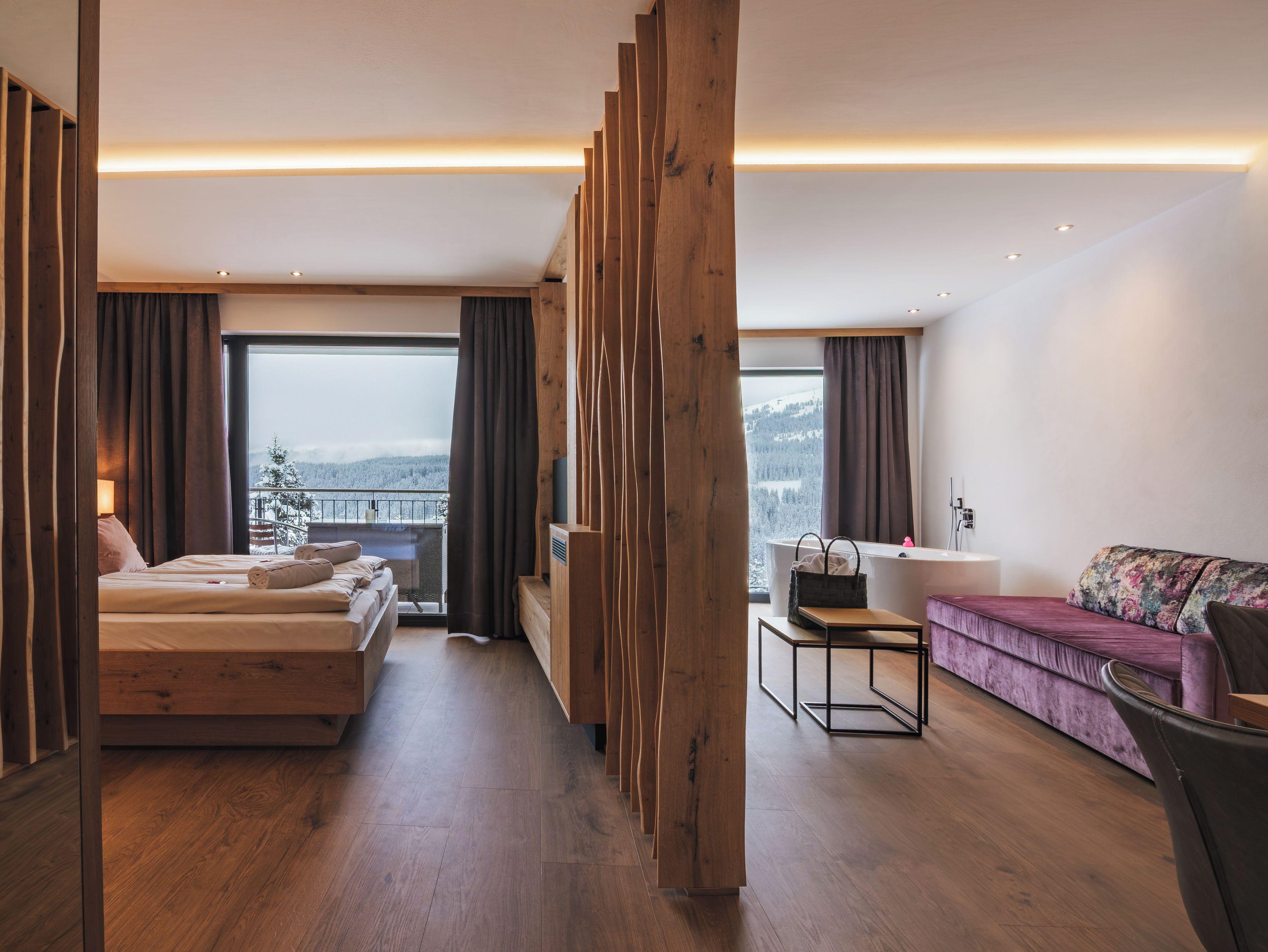 A modern hotel room with a bed, a sofa, a desk, and a view of a snowy landscape.