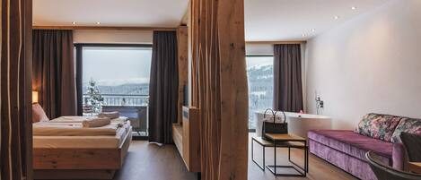 A modern hotel room with a bed, a sofa, a desk, and a view of a snowy landscape.