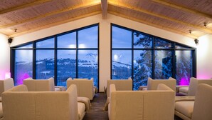 Une pièce dotée de grandes fenêtres offrant une vue sur les montagnes enneigées, de poutres en bois au plafond et de fauteuils beiges recouverts de tissu.