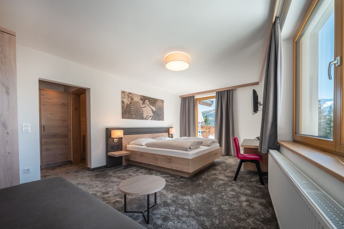 Una habitación de hotel moderna con una cama grande, una mesita pequeña, un escritorio y vistas al exterior.