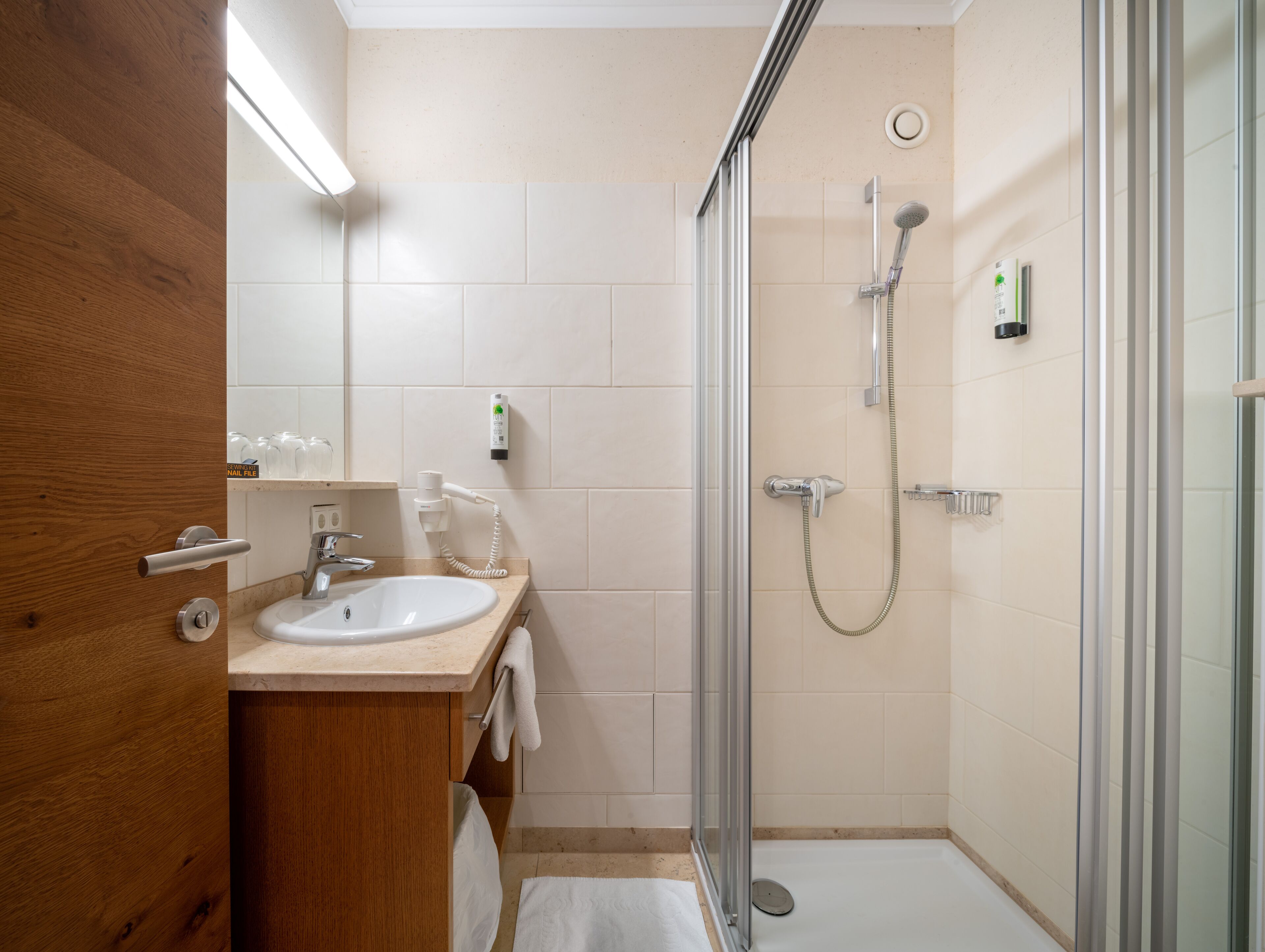 Une salle de bain moderne avec un meuble-lavabo en bois, un évier, un miroir et une douche séparée par une paroi de verre.