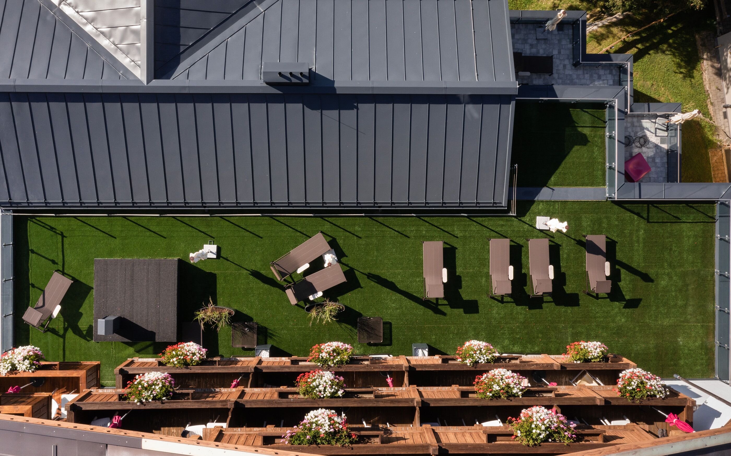 Vista aérea de una terraza en la azotea con varias zonas de estar, una piscina pequeña y jardineras con flores.