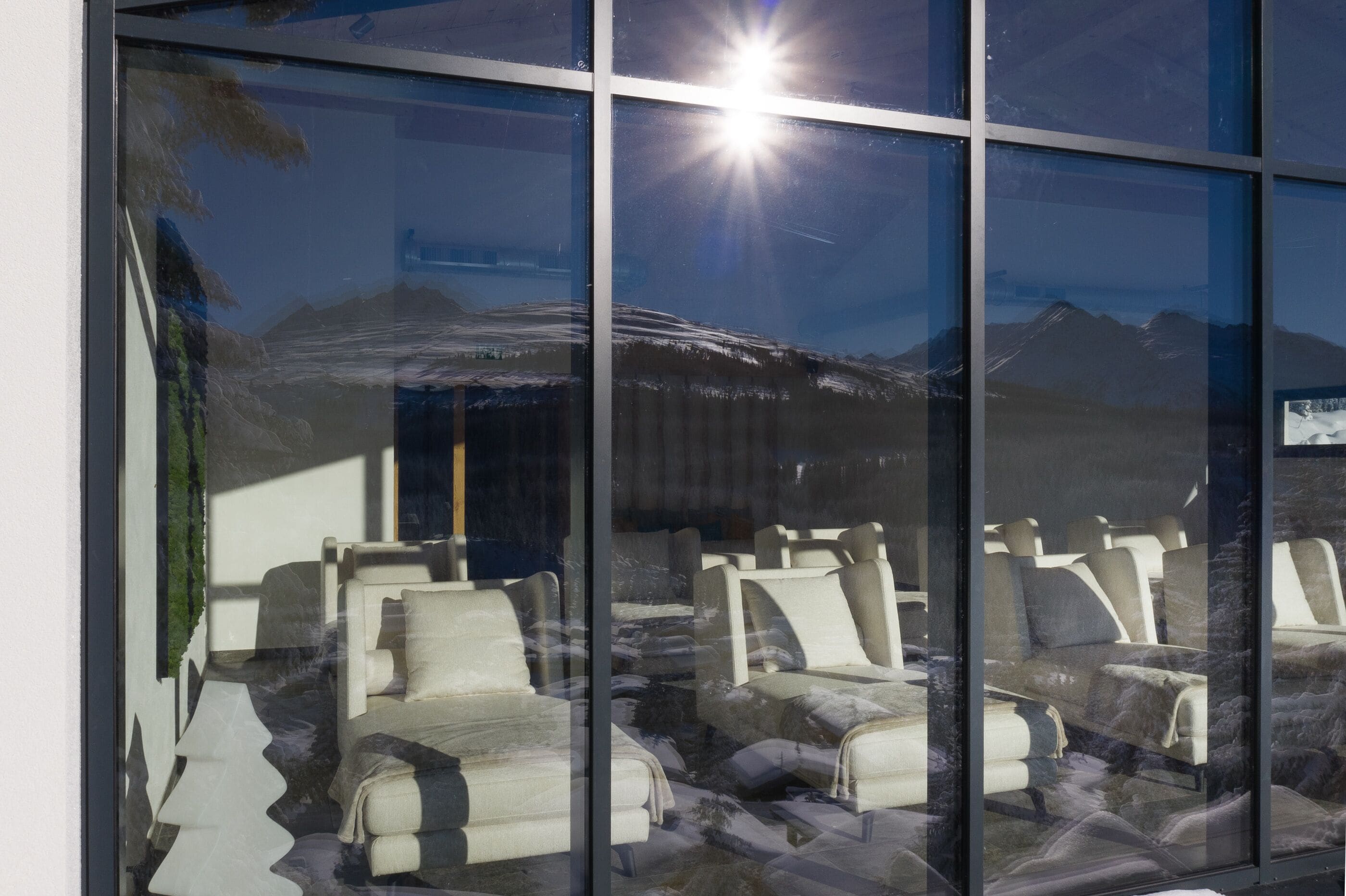 A room with multiple seating areas, a large window reflecting a mountain view, and a bright light source outside.