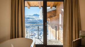 Une pièce avec un plafond en bois, une porte vitrée donnant sur un balcon avec vue sur la montagne et une chaise.
