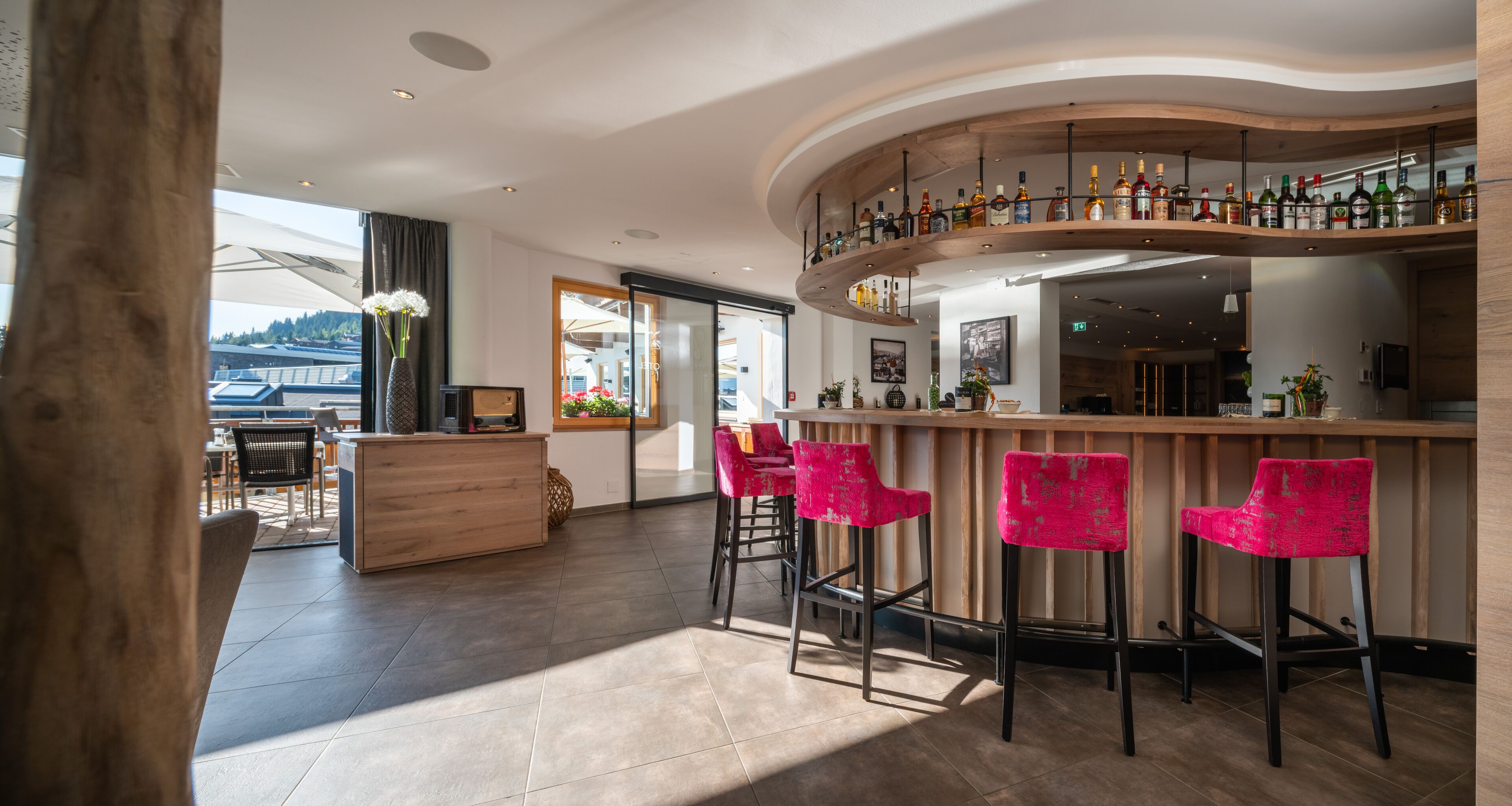 Eine moderne Bar mit einer gebogenen Holztheke, drei roten Barhocker und einer Auswahl an Spirituosenflaschen.