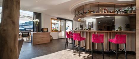 Eine moderne Bar mit einer gebogenen Holztheke, drei roten Barhocker und einer Auswahl an Spirituosenflaschen.