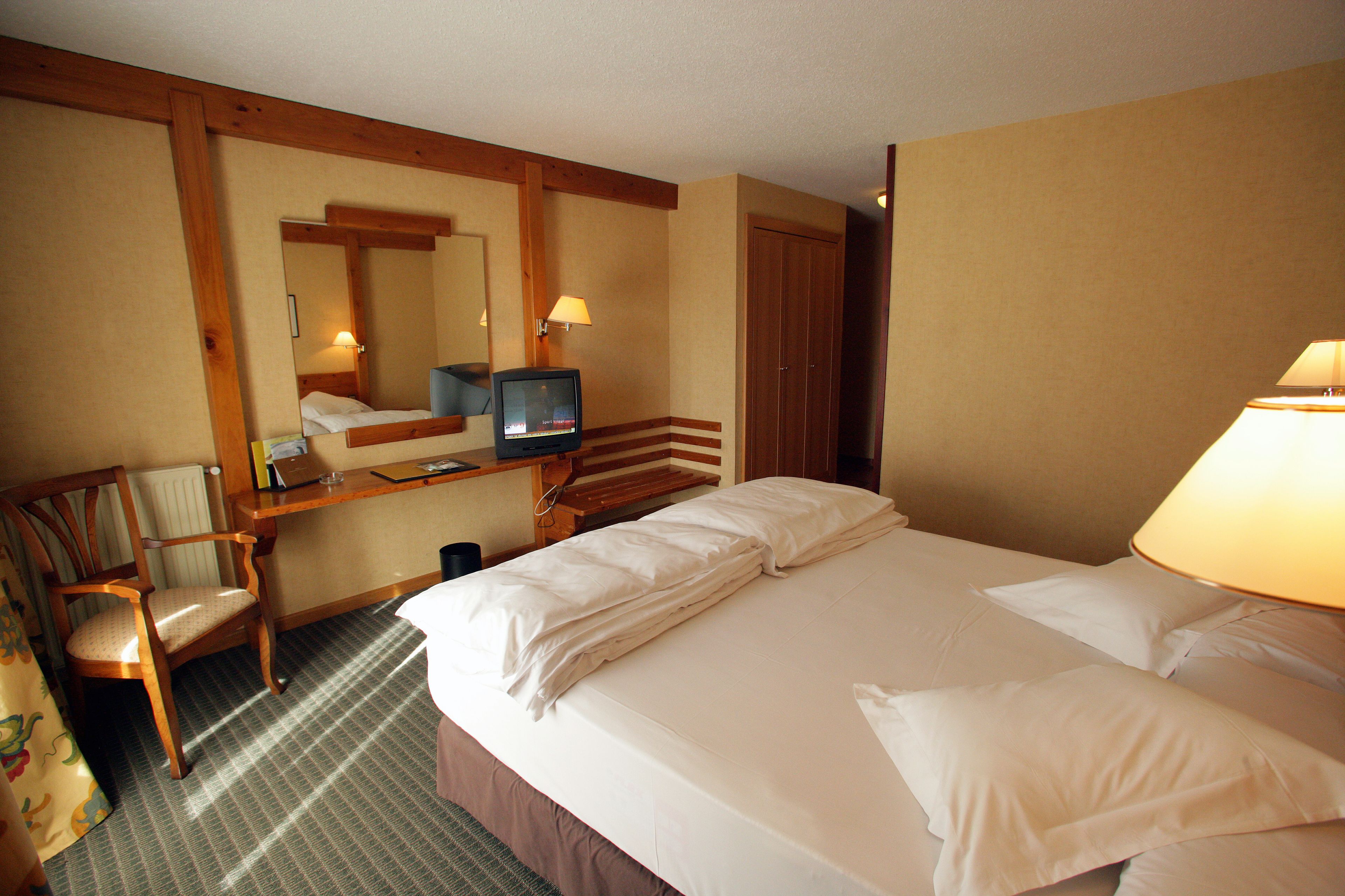 A hotel room with a bed, a desk, a chair, a television, and a lamp.
