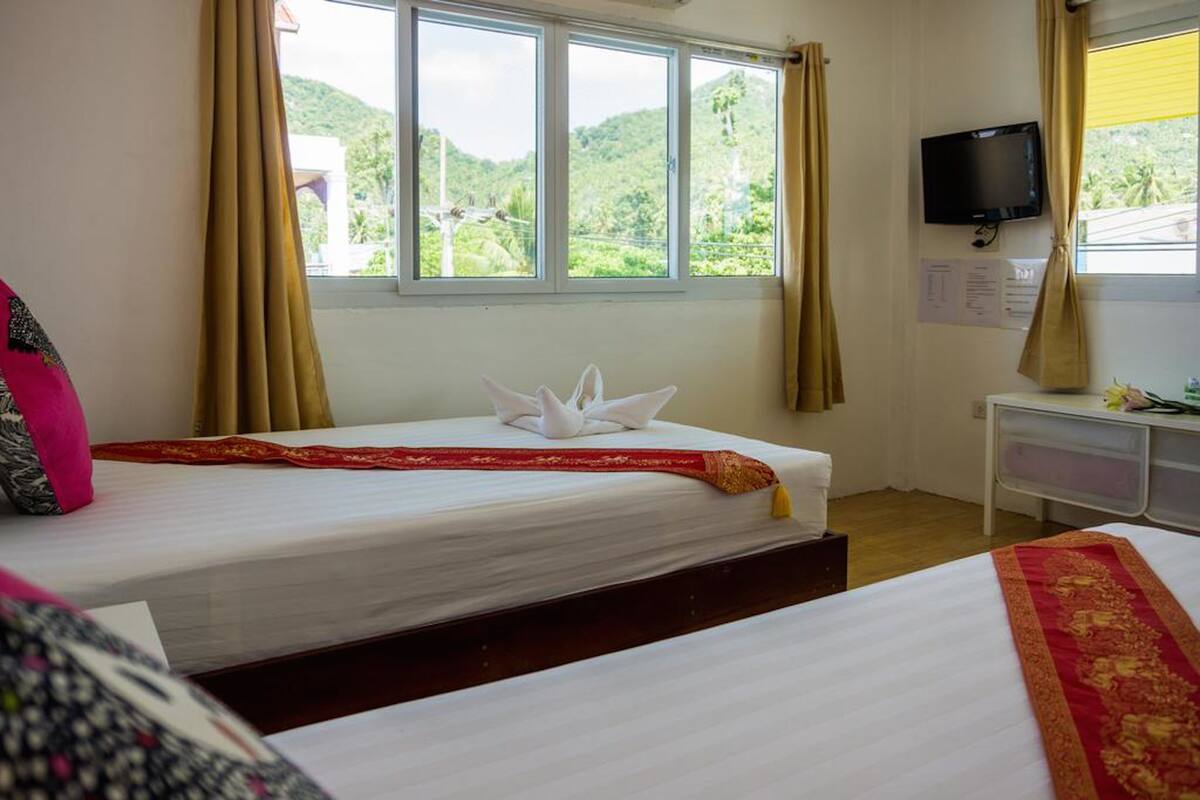 A hotel room with two beds, a television, and a window with curtains.